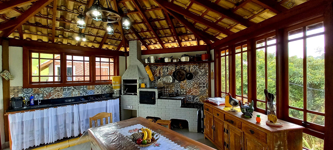 Cozinha compartilhada do Recanto Feliz com fogão a lenha, mesa de madeira e vista para a mata